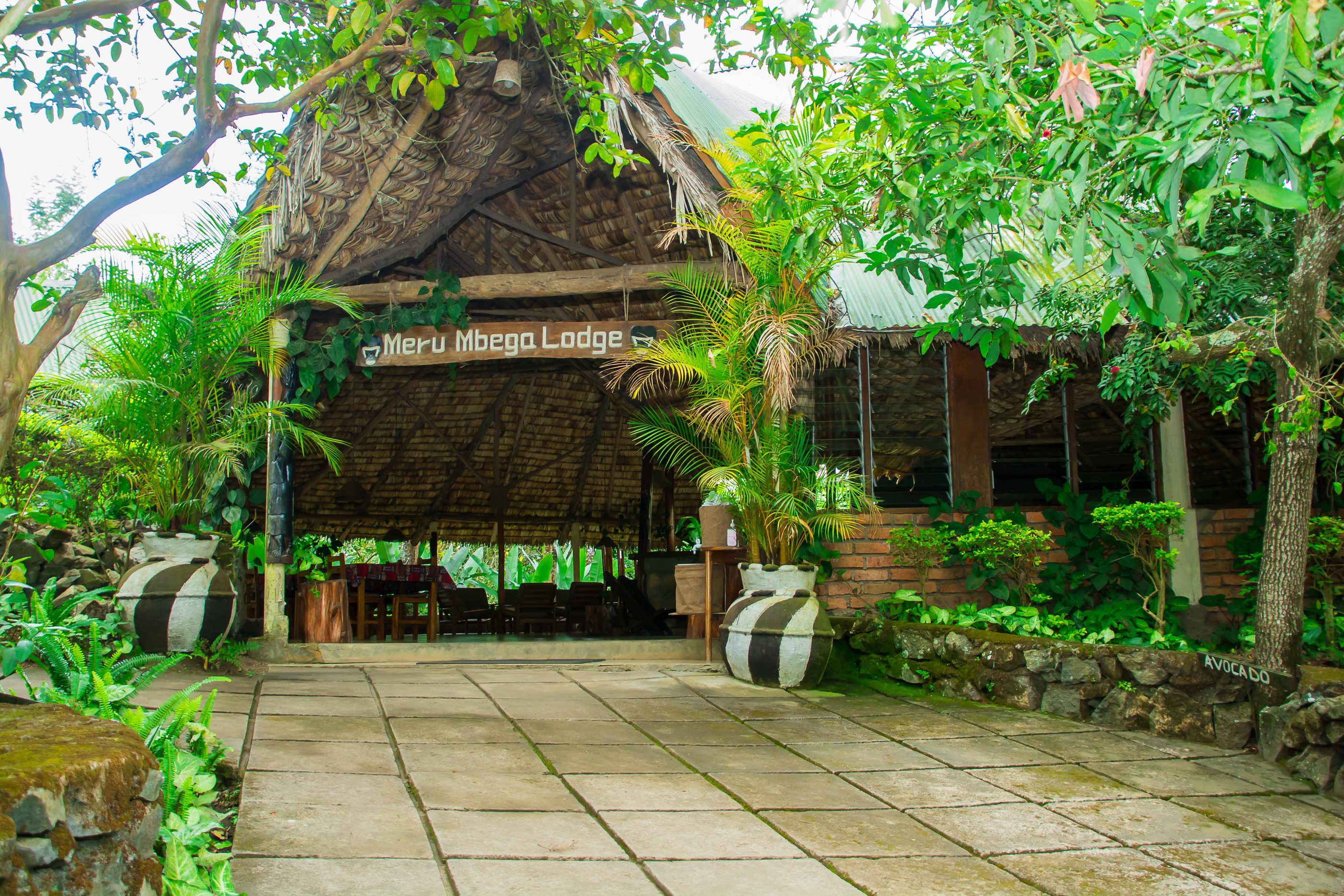 Das reetgedeckte Haupthaus der Meru Mbega Lodge inmitten tropischer Gärten