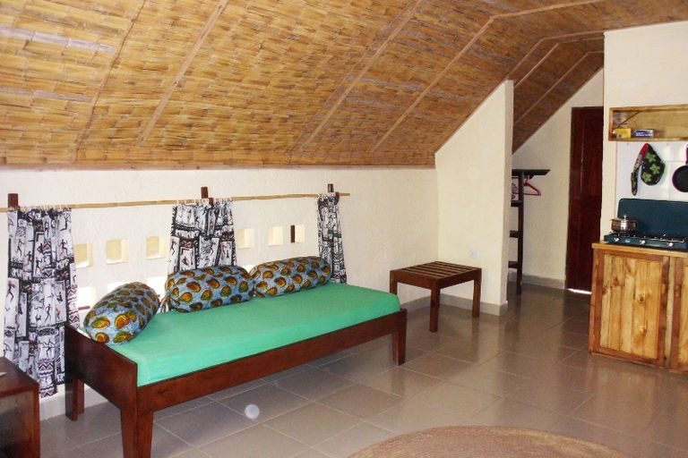 Room with a green bedspread under a thatched ceiling