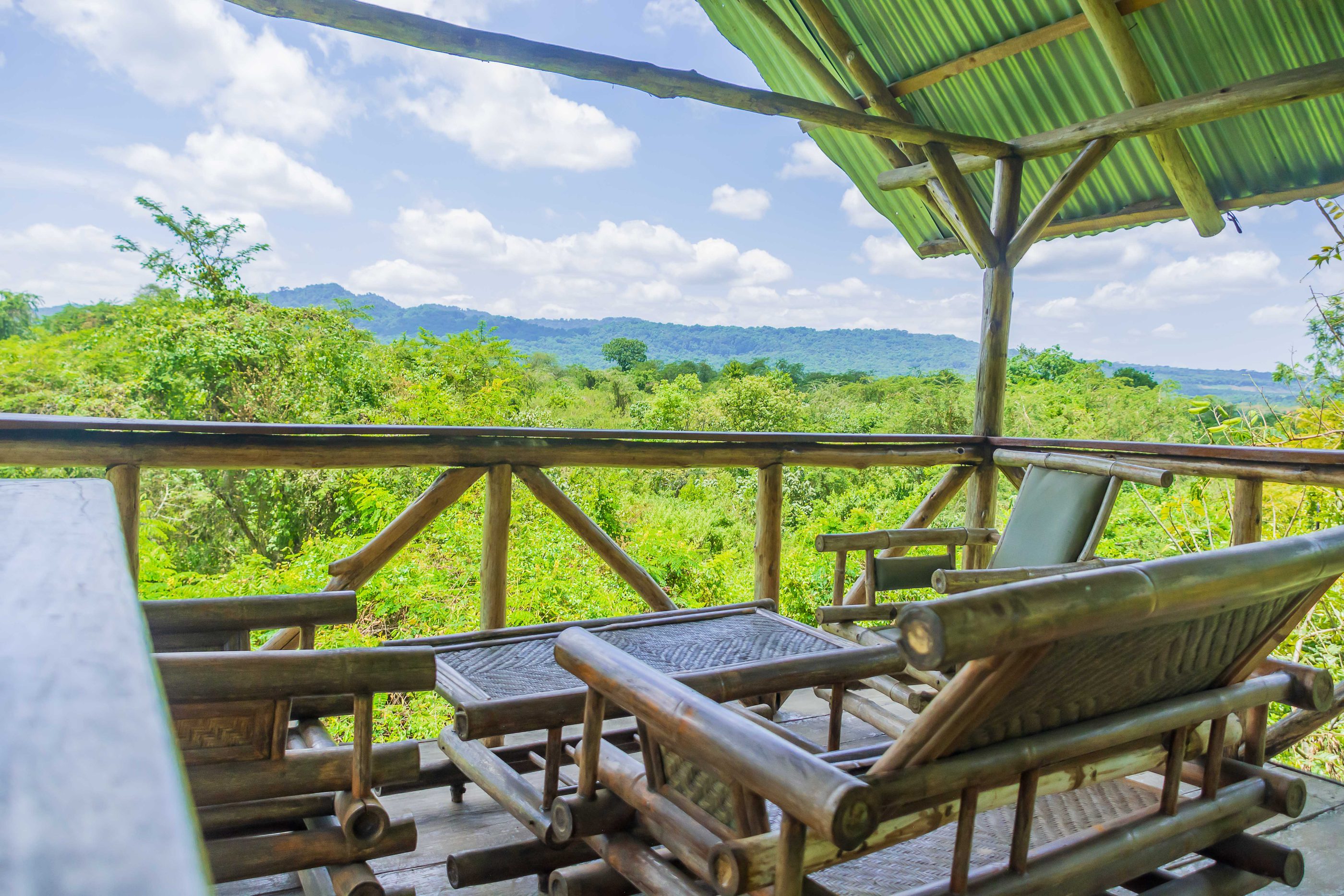 Bambusliegen auf einer schattigen Terrasse der Lodge, mit Blick über den Wald bis zu den Hügeln